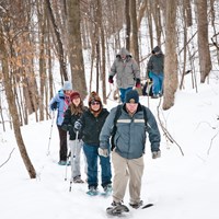 A group of people in winter hats snowshoes along a snow-covered trail in the forest.