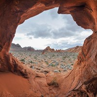 Looking out of a cave in a rock formation out into a desert landscape.