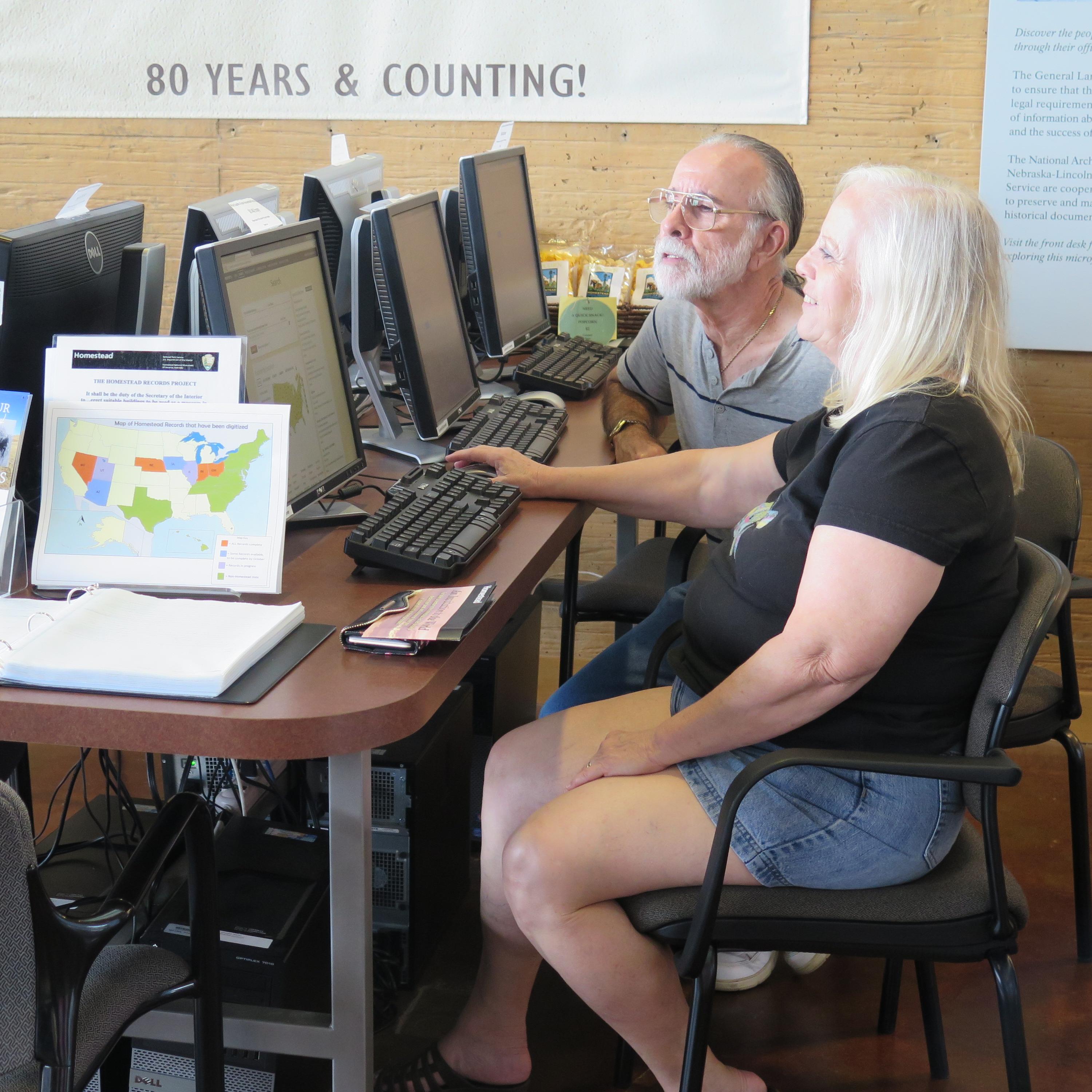 Two people sitting down and looking at records on computers