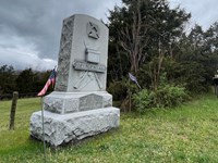 Large granite monument inscribed with 128th Reg NYSVI next to a row of trees.