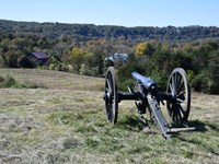 Cannon on a grassy knoll overlooking fall foliage and a historic farm.