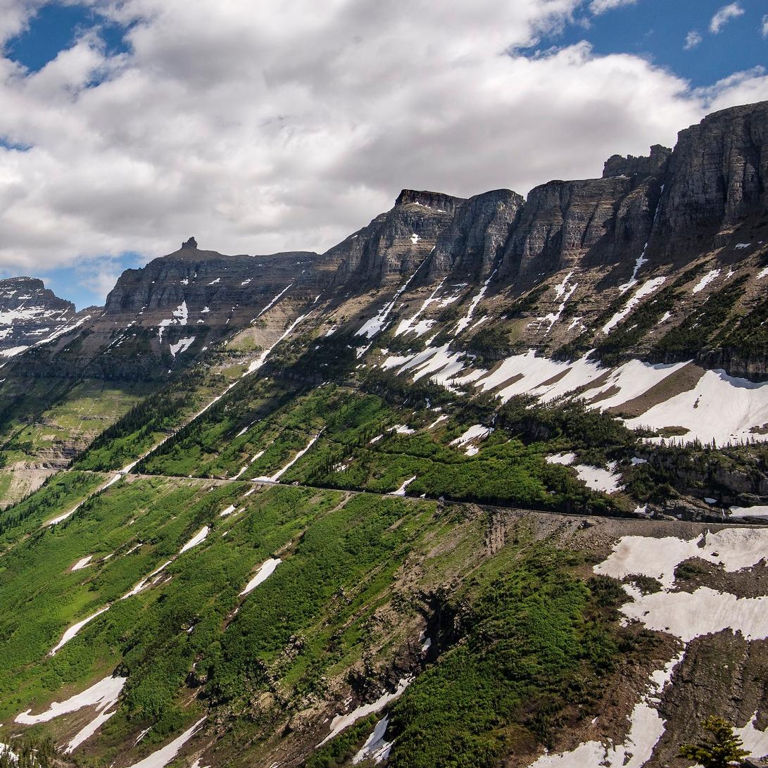 Line of road streaks across mountain side with snow patches