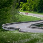 Winding road with green grass on both sides. Red Car driving on road in the distance towards viewer.