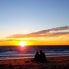 The silhouettes of two people on the beach facing a brilliant sunset.
