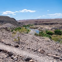 A trail winds above on a high vista overlooking a small stream.