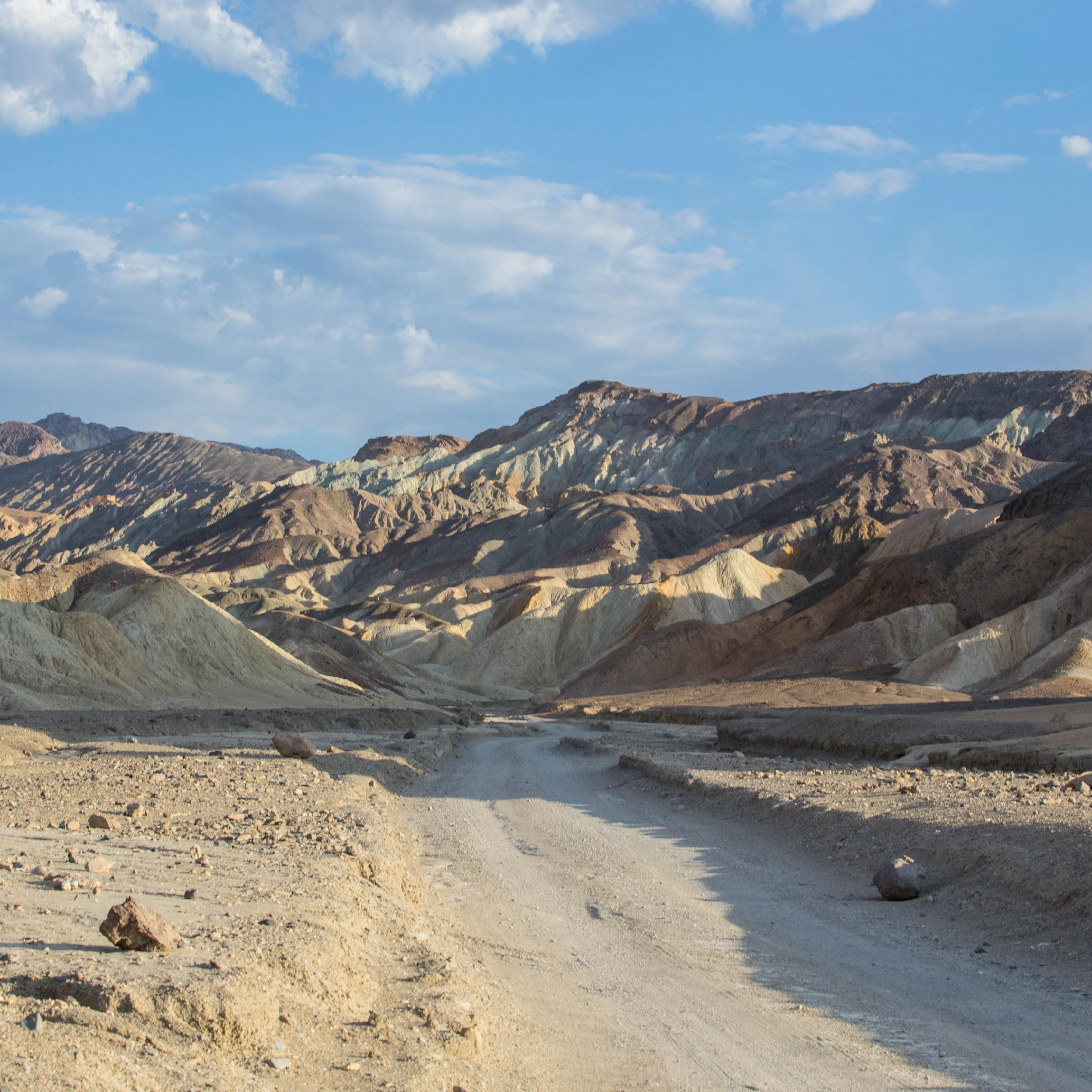 A dirt road through bare brown and yellow striped hills.