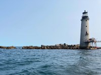 View of the rocky island looking up from the water with the grey lighthouse on the right