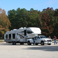A large white pick up truck pulling a 5th wheel camper is parked in parking lot.