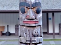 Close up of a portion of a totem pole with a building in the background