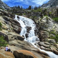 A person sits on rounded rocks at the base of Tokopah Falls.
