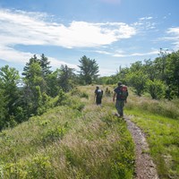 Two people with backpacks hike along a ridge top trail 