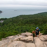 person climbing up rocks with a ocean view in the distance
