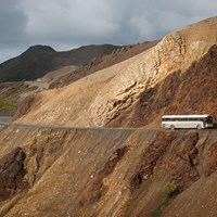 a bus driving on a dirt road on the side of a mountain