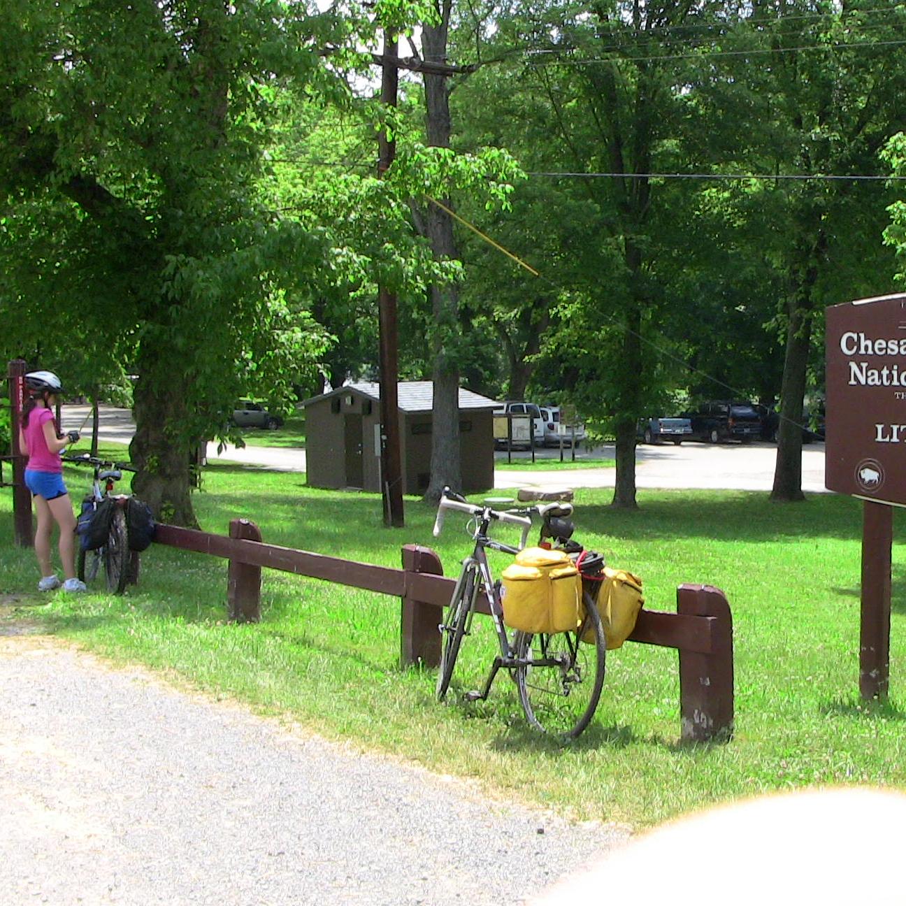 bicyclists stopped along a natural surface path near a modern and an historic historic