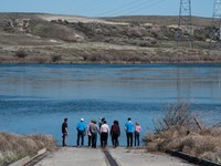 Color photograph of a group of six people at the bottom of a ramp looking across a river.