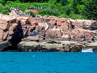 People gather on stairs leading down a cliff from a road to the ocean
