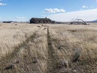 Color photograph of a large house at the end of a large field of tall tan grass