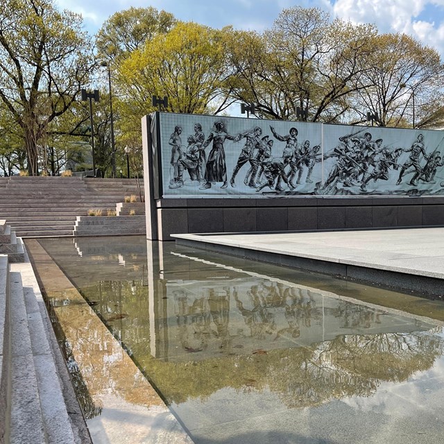 A pool of water in front of a wall depicting World War I soldiers.