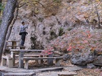 A man use a camera near an open cave feature with stone benches and tables.