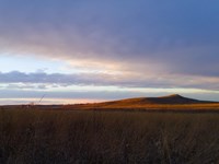 Photograph taken at dusk, with a dramatic purple sky and waves of grass. Spirit Mound is visible