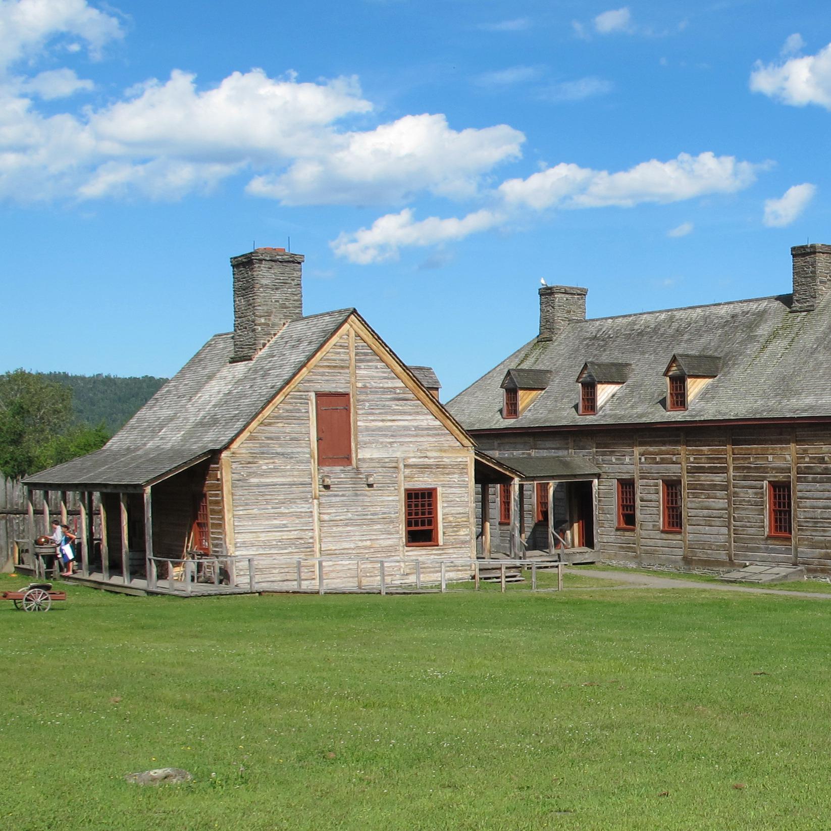 Reconstructed historic wood buildings on a lawn.
