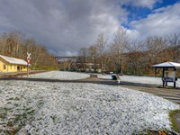 Yellow train station & tracks to left of distant arched bridge in snow, three-sided kiosk at right.