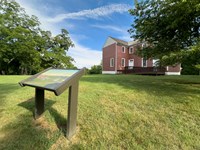 A park sign on a lawn in front of a 2-story red house.
