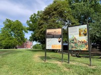 Two upright interpretive signs in front of a 2-story red plantation house.