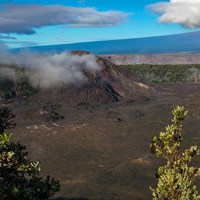 Volcanic crater with a large cinder cone on the left-hand side and a larger mountain beyond.