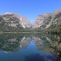 A lake sits at the base of a mountain canyon with a near perfect reflection on its calm surface.