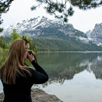 A woman takes a picture beside a lake.