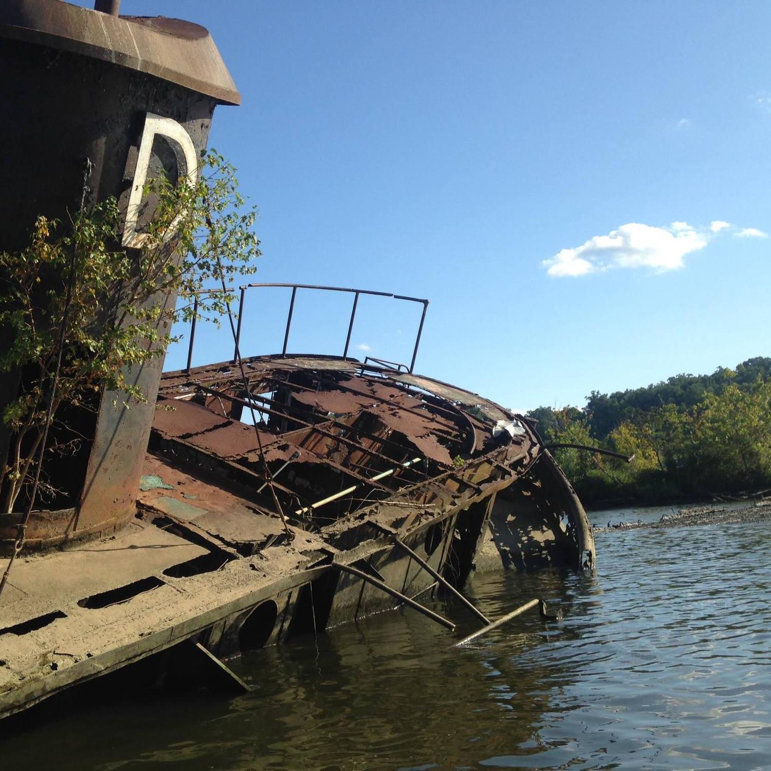 A rusty old metal ship with a large letter D sits half sunk in a waterway. 