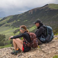 Two hikers sit on a ridgeline taking in views of the valley below.