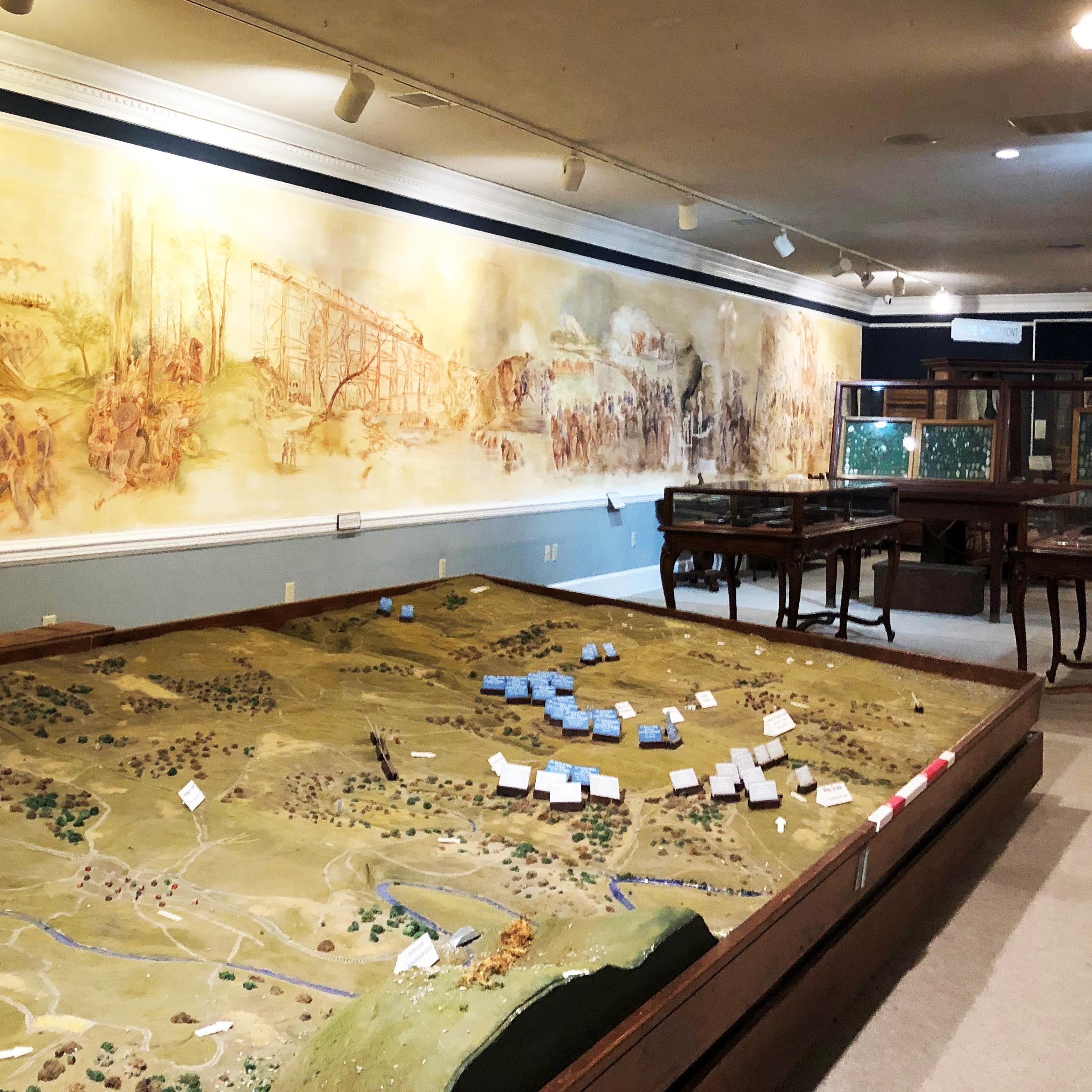 A museum exhibit hall has a battlefield diorama and mural painting.