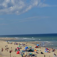 A crowd of people enjoy a wide sandy beach under light clouds and a blue sky.