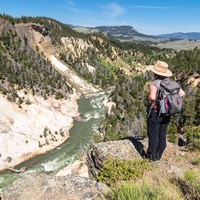 A hiker stands on the edge of a canyon and looks down at the river below.