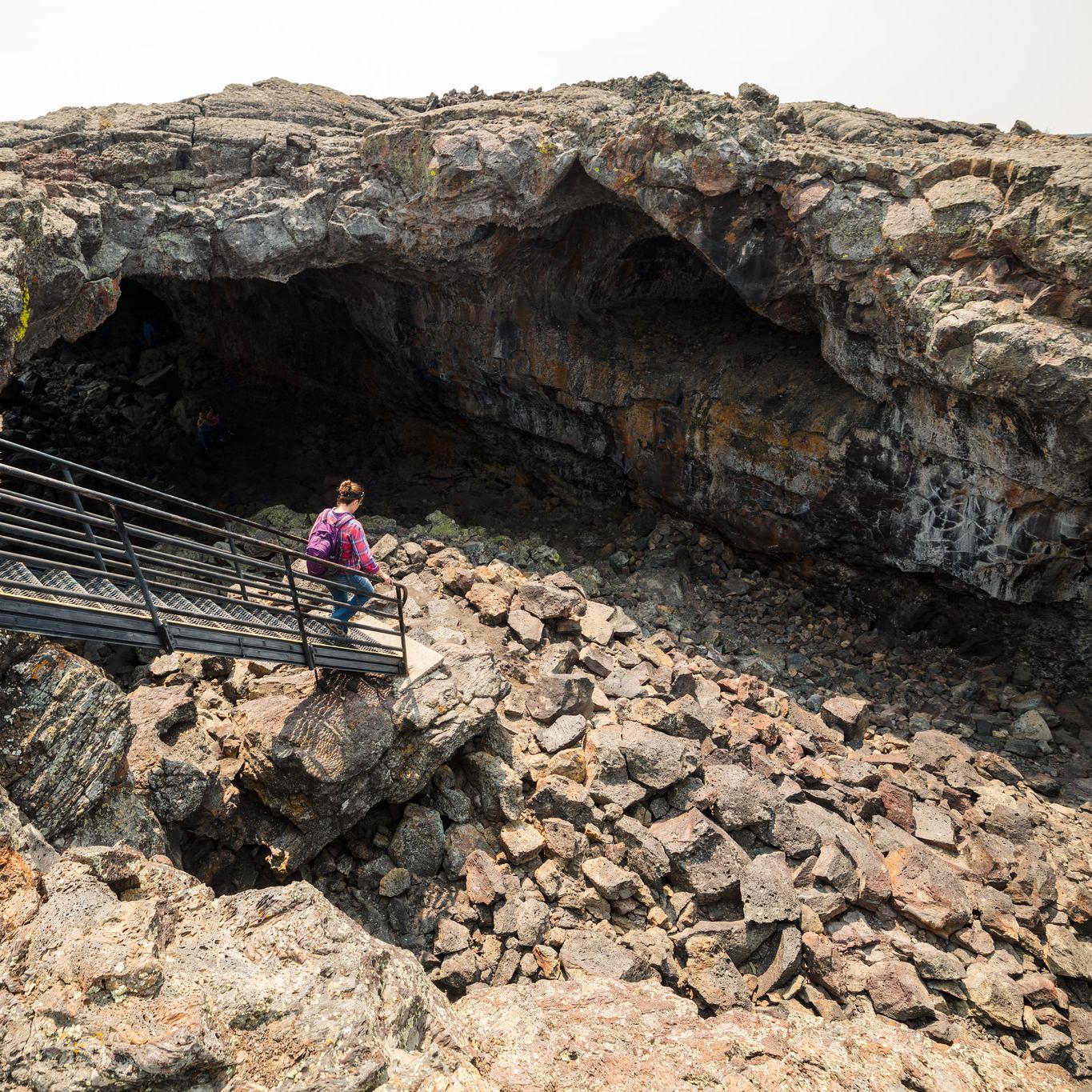 A person walks down a set out stairs into the wide open entrance of a lava tube.