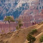 HIkers walk along a descending slope surrounded by red rocks