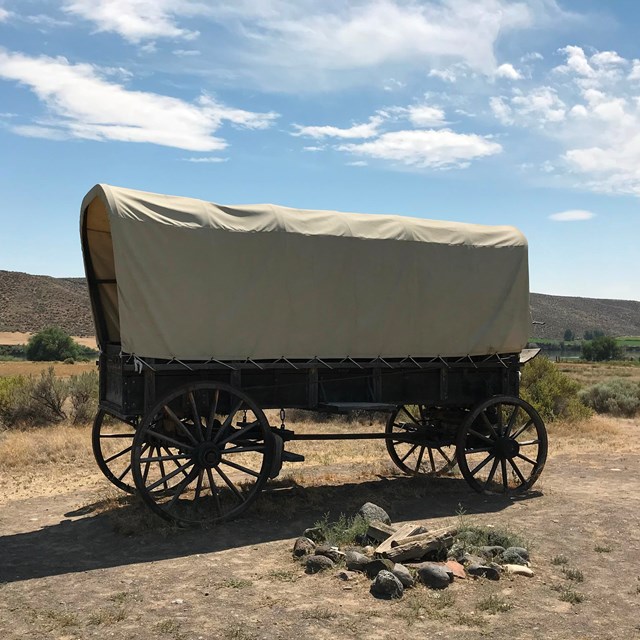 A large covered wagon in a flat desert.