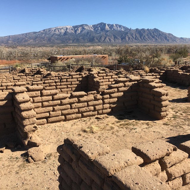 Ruined adobe walls with distant desert mountains.