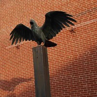 A statue of a raven sitting atop a plinth stands outside a three story brick house.