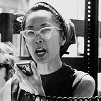 Asian woman with cat-eye glasses holding megaphone speaker.