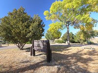 A brown entrance sign sits at the entrance to a grassy park with a trees.