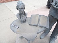 A bronze statue consisting of a bust, book, and pair of glasses on a table.