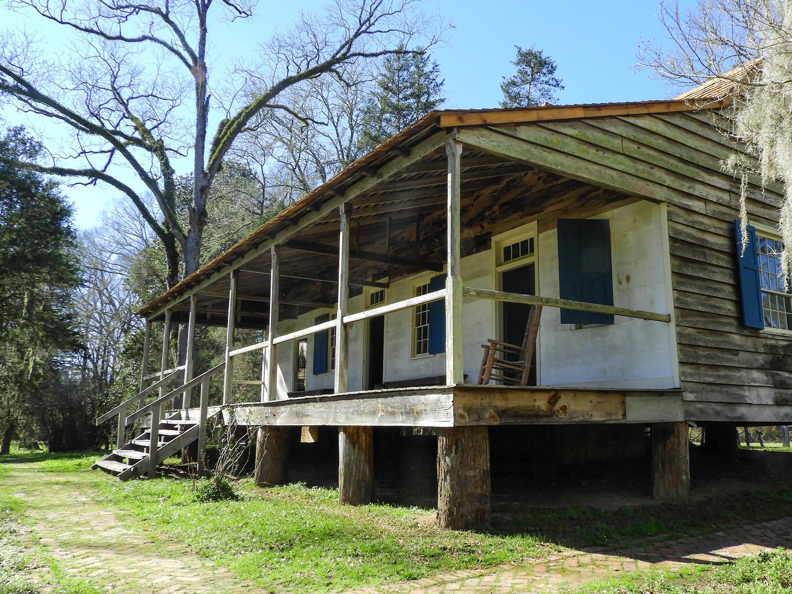 Side perspective of a wooden home with a covered porch and a white front exterior and blue shudders 