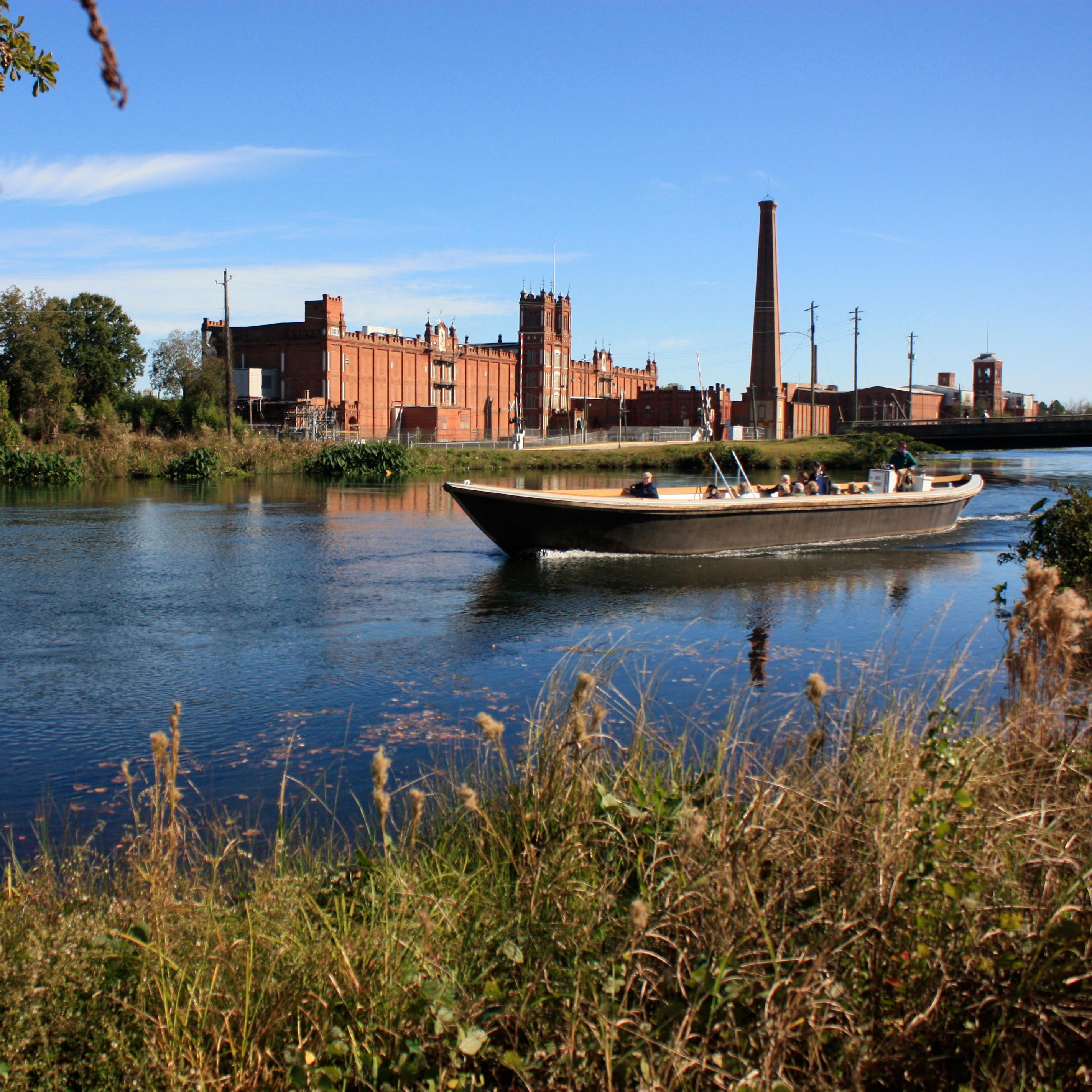 Tour boat going down canal with brick mill in background