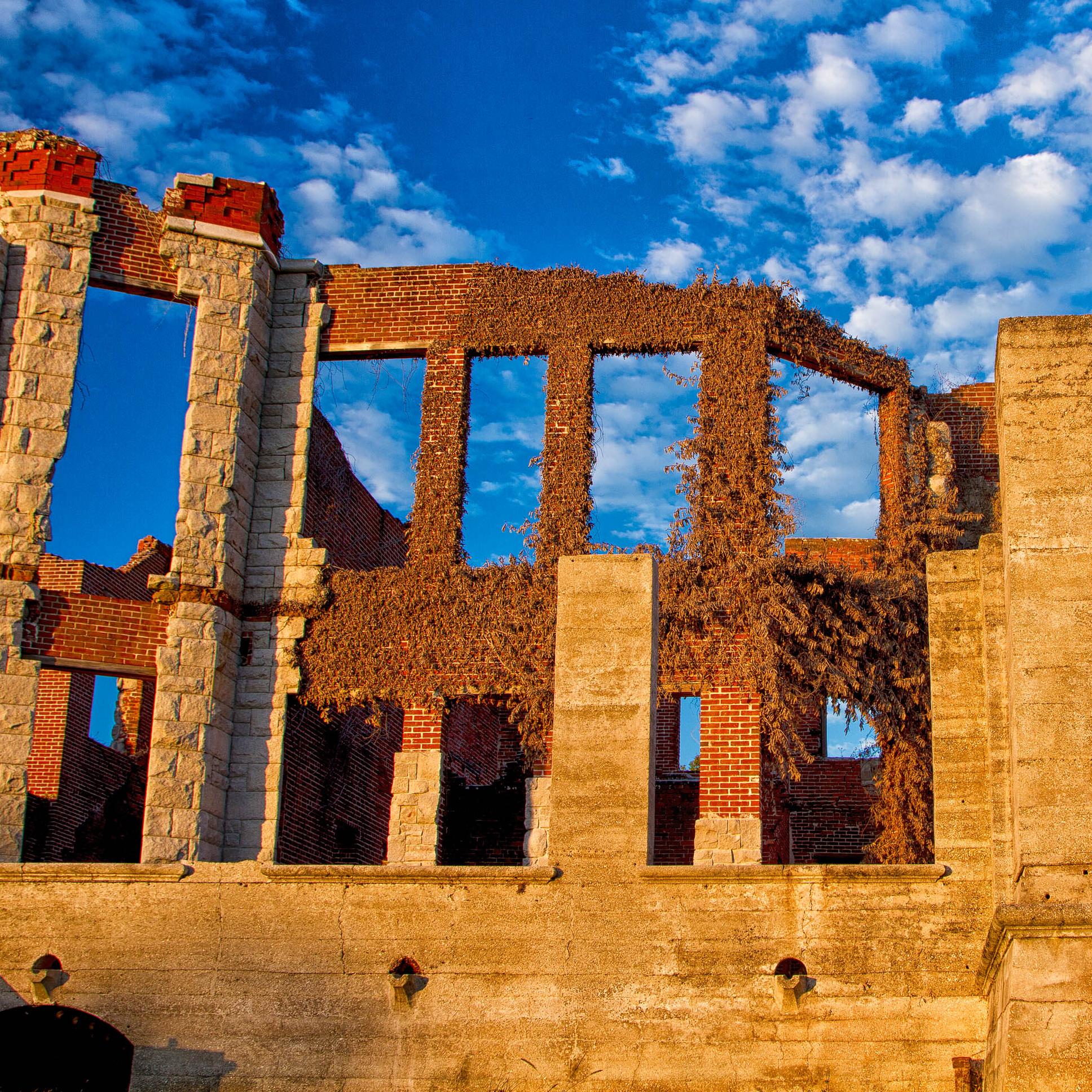 Burnt out ruins of a brick and stone mansion. The blue sky can be seen through empty window frames.