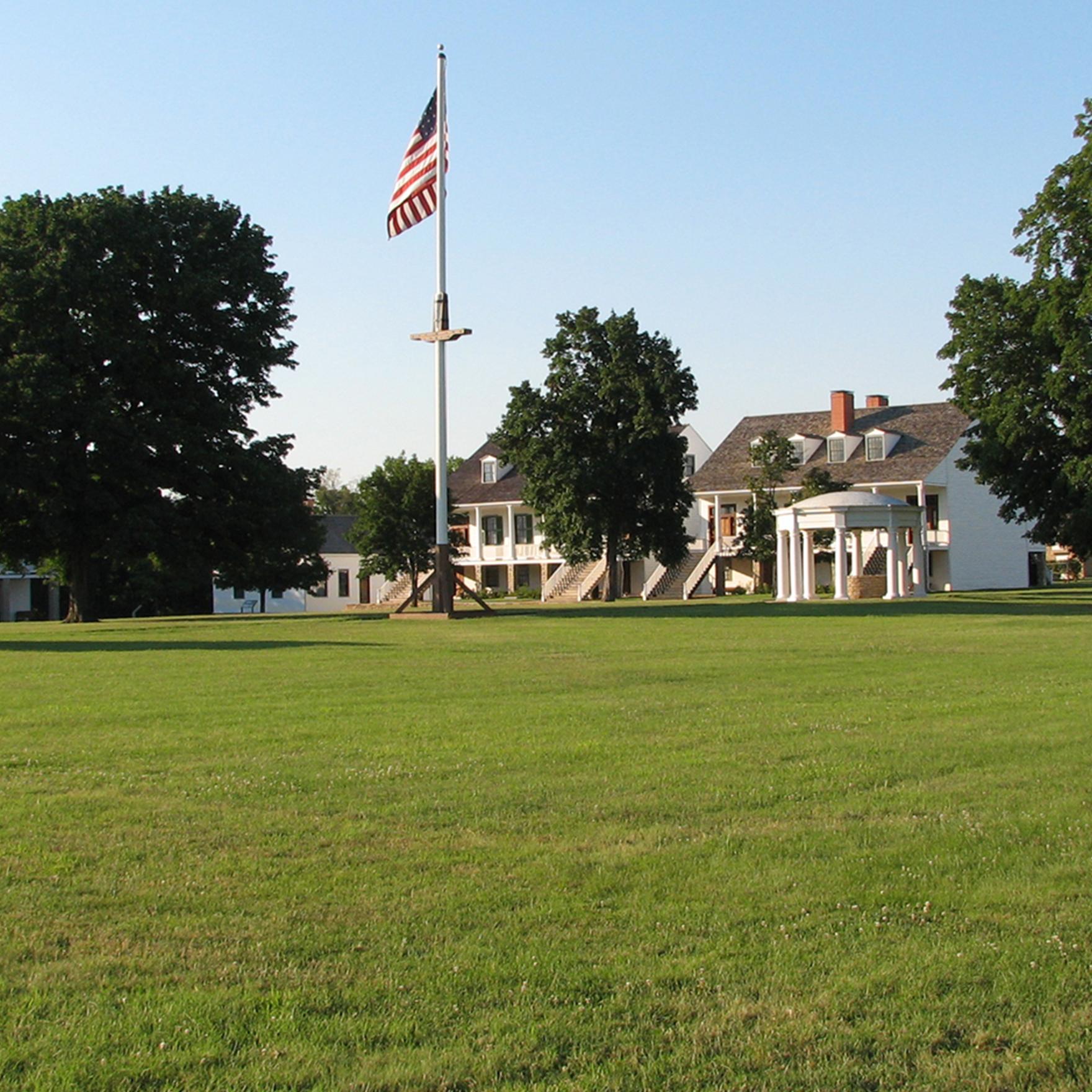 buildings, trees, and grassy area.  flag pole in middle.