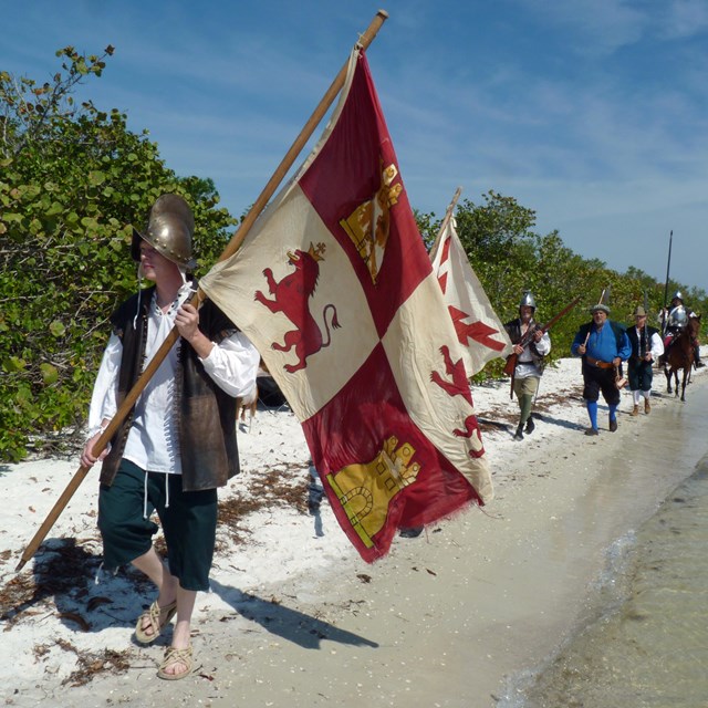 Living history participants dressed as explorers walk a beach