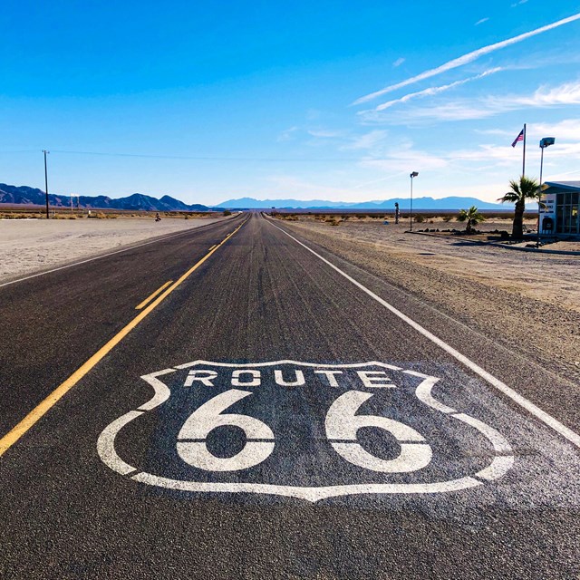 A route 66 logo on a two lane highway in the desert.